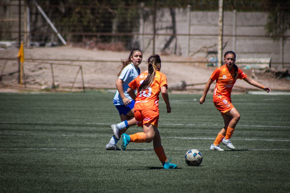 Imagen dinámica de un partido de fútbol femenino, que muestra a las jugadoras en pleno movimiento sobre un campo al aire libre.