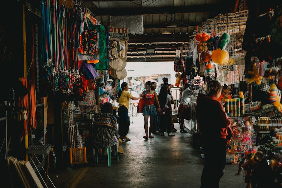 Escena animada de un mercado cubierto, con compradores explorando diversos puestos repletos de colorida mercancía.