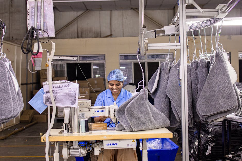 Un trabajador de fábrica cosiendo textiles en una máquina industrial en una moderna planta de fabricación de prendas de vestir.