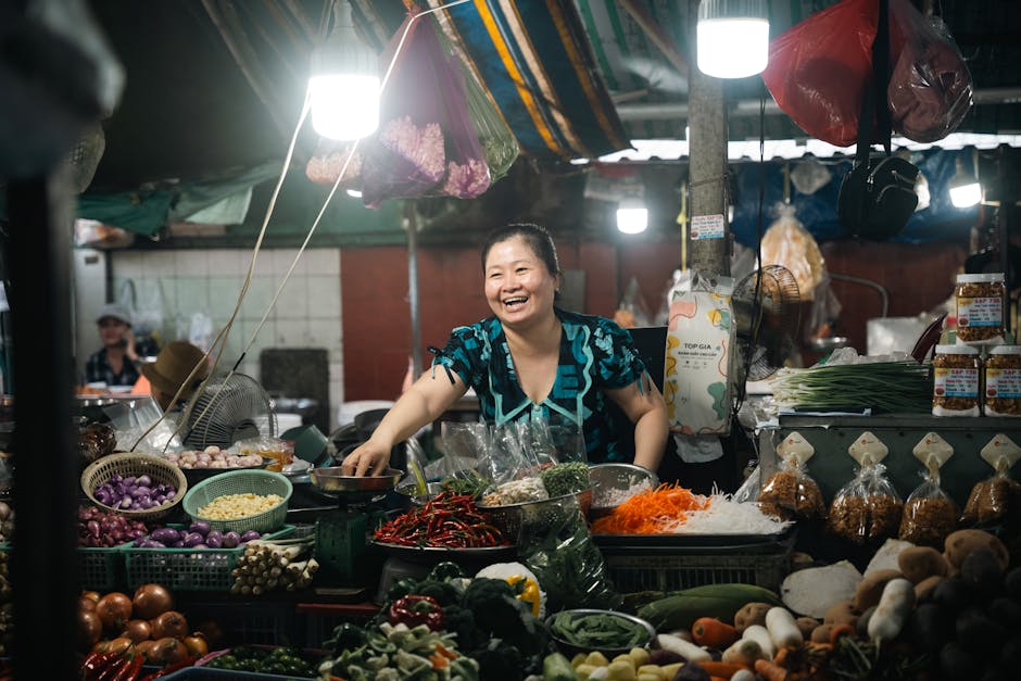 Vendedora sonriente en un puesto de un mercado asiático, exhibiendo verduras y especias frescas.