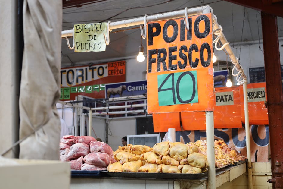 Puesto de mercado que exhibe pollo y cerdo frescos con carteles de precios en español.