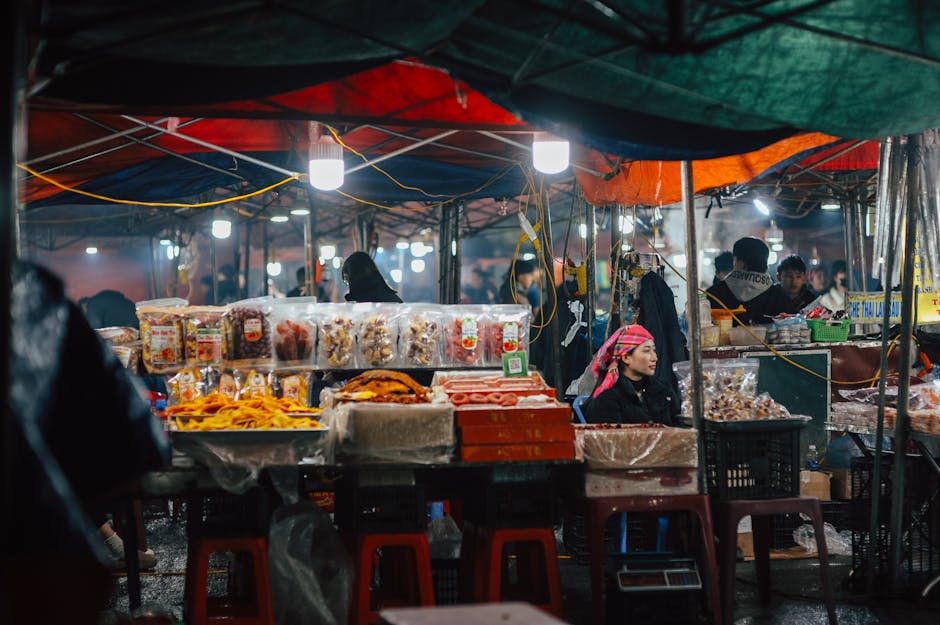 Una animada escena de mercado nocturno con vendedores que ofrecen diversos productos alimenticios, iluminado por luces de colores.