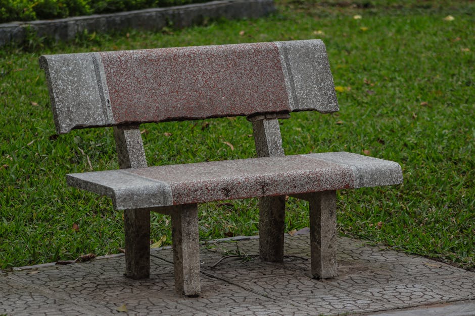 Un banco de piedra solitario en un parque vacío con césped verde y exuberante.