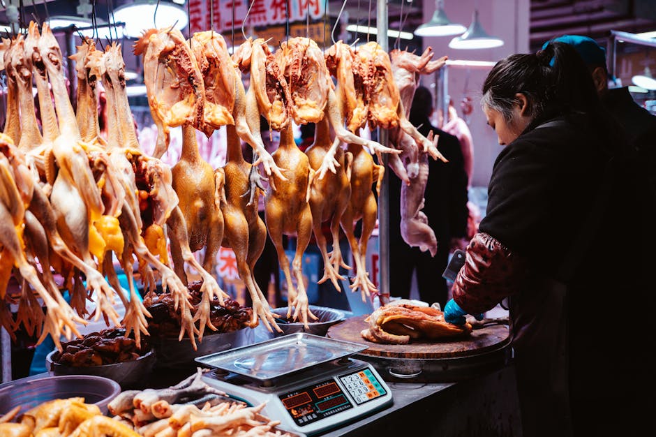 Un vendedor prepara aves de corral en un mercado asiático tradicional interior con pollos colgados.