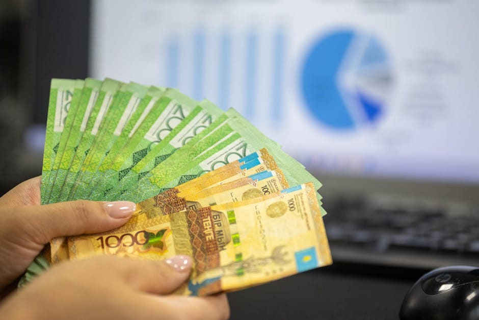 Primer plano de manos sosteniendo billetes de tenge kazajo con gráficos financieros de fondo.