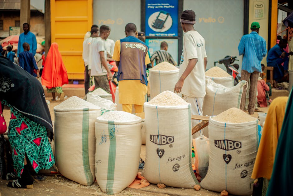 Bullicioso mercado al aire libre con gente y grandes sacos de arroz, entorno comunitario vibrante.