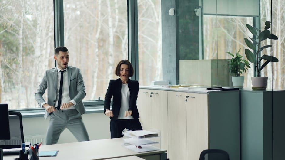 Dos adultos bailan en un moderno espacio de oficina con grandes ventanales.