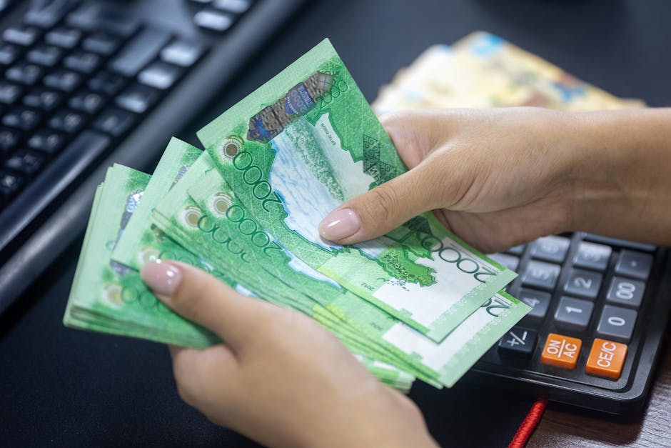 Primer plano de manos contando billetes de tenge kazajo con calculadora en un entorno de oficina.