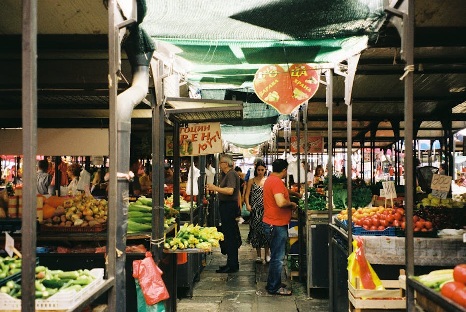 Un animado mercado de agricultores al aire libre con verduras frescas y gente comprando en un día soleado.