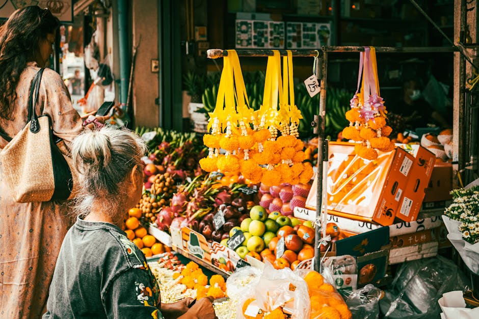 Colorida exhibición de frutas y guirnaldas de flores en un bullicioso mercado callejero de Bangkok.