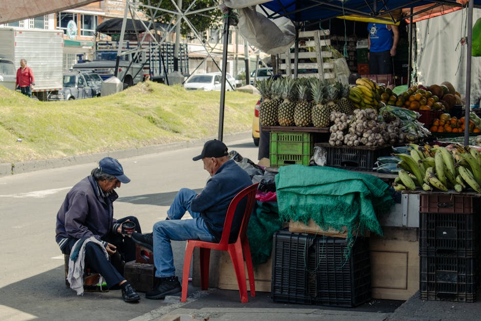 Dos vendedores ancianos en un mercado callejero vendiendo frutas y verduras tropicales.