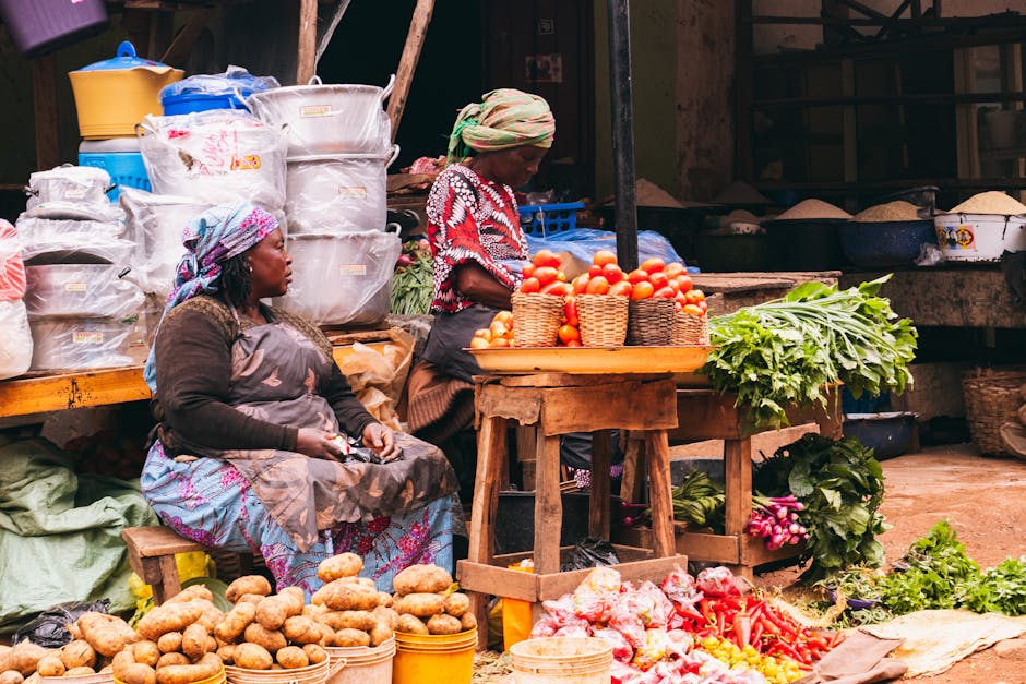 Colorida escena de mercado en Jos, Nigeria, que muestra mujeres vendiendo productos frescos con verduras y cestas de colores vibrantes.