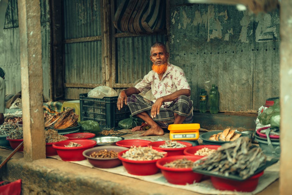 Vendedor anciano que vende productos secos en un vibrante mercado callejero de Bangladesh.