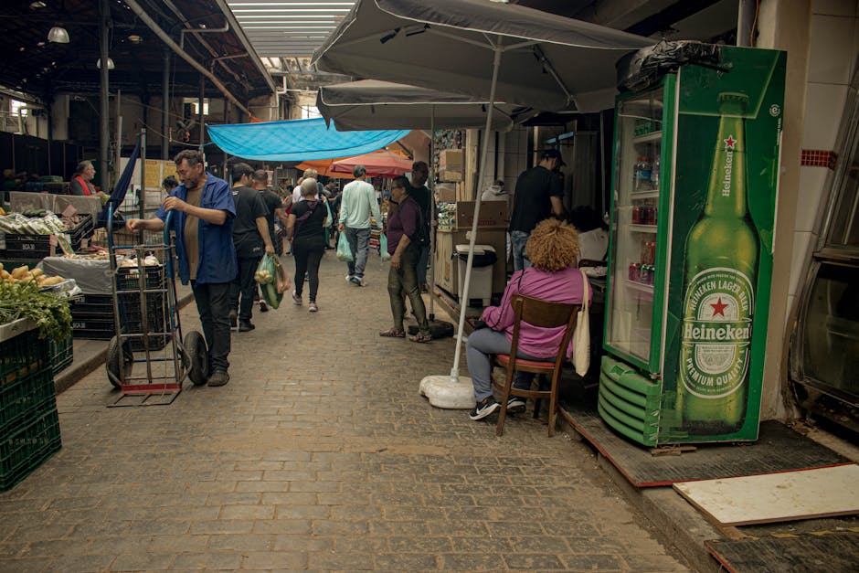 Escena de un animado mercado cubierto con gente comprando y un expositor de Heineken.