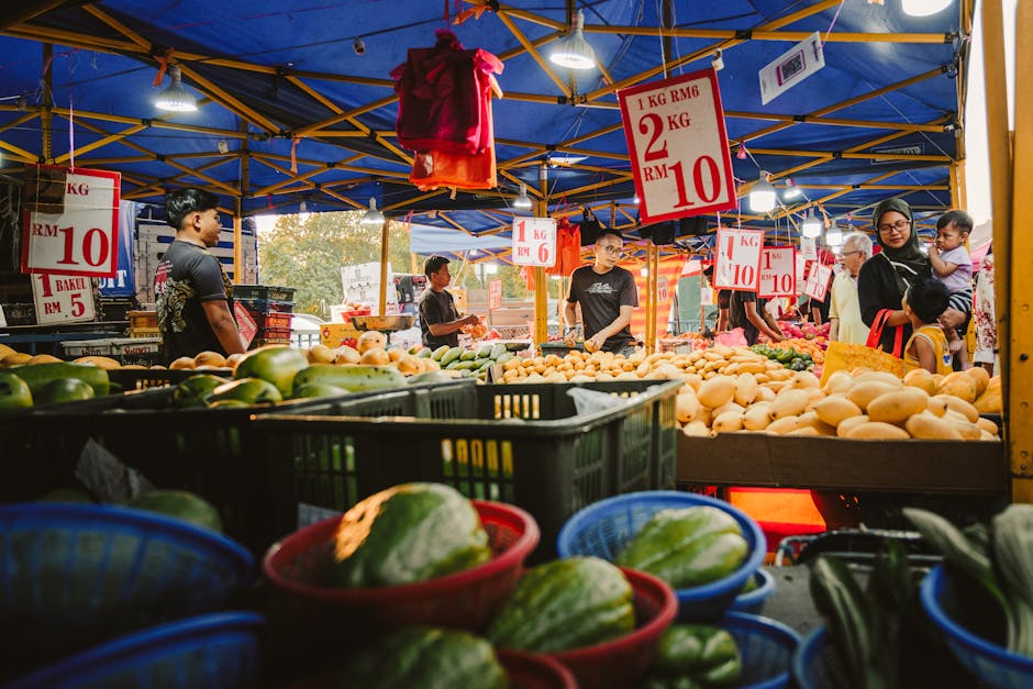 Un bullicioso mercado nocturno en Sepang, Malasia, que exhibe una variedad de productos frescos bajo coloridas luces de toldos.