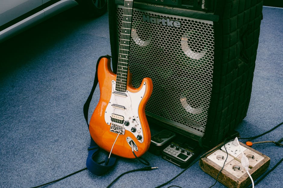 Guitarra eléctrica naranja apoyada contra un amplificador Hartke al aire libre, mostrando la configuración del equipo musical.