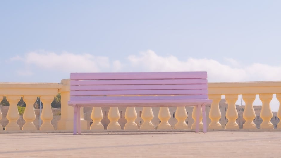 Un banco rosa sereno en un soleado paseo marítimo de Malta, perfecto para relajarse y hacer turismo.