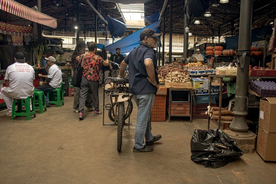 Un animado mercado cubierto donde vendedores y clientes interactúan entre productos y artículos frescos.