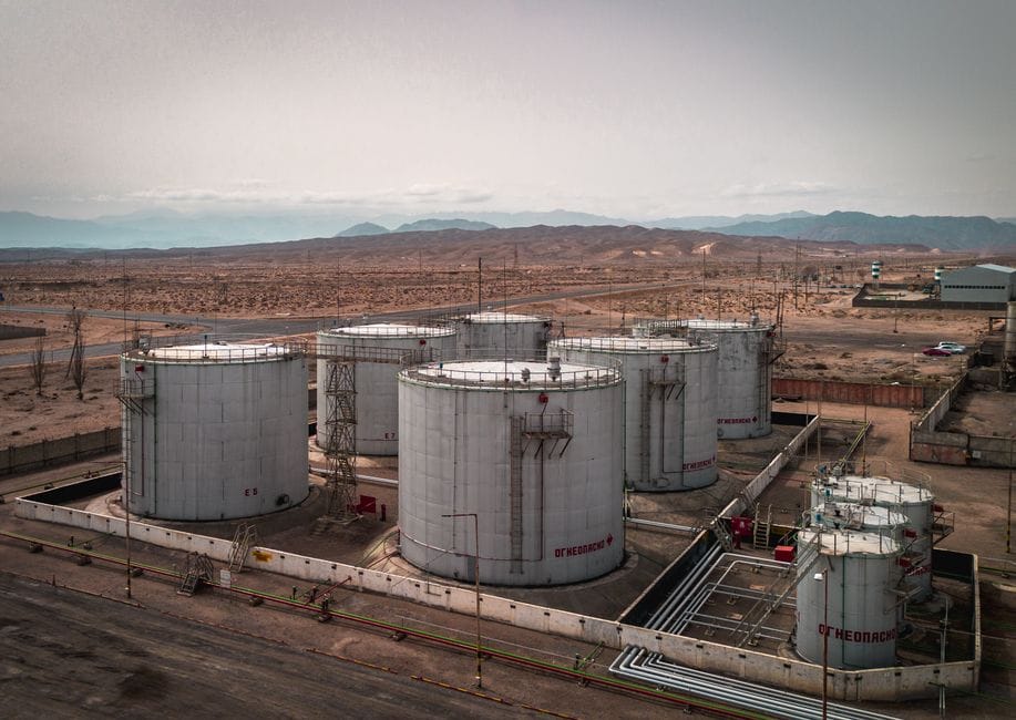 Vista aérea de grandes tanques de petróleo industriales en un entorno desértico con montañas en la distancia.