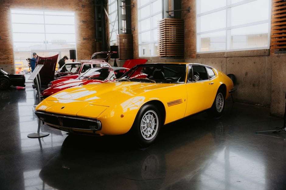 Un automóvil deportivo Maserati vintage de color amarillo brillante exhibido en el interior de una sala de exposición de automóviles.