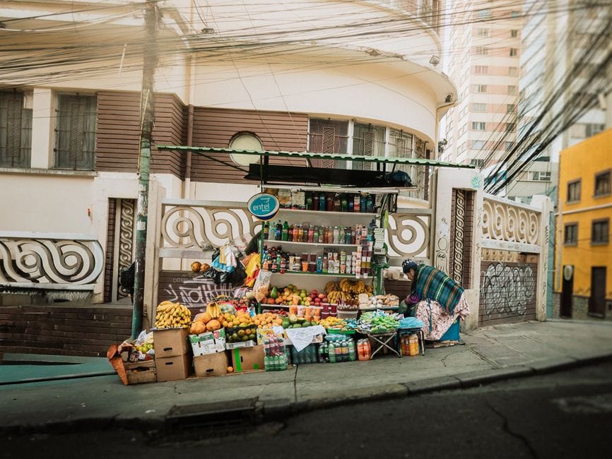 Puesto callejero lleno de vida en Bolivia que vende productos frescos, exhibiendo frutas coloridas y productos envasados.