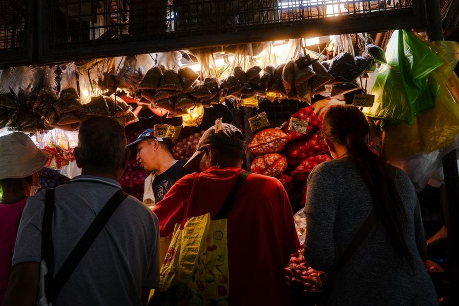 Un animado ambiente de mercado con gente comprando especias y productos agrícolas en un puesto cubierto.