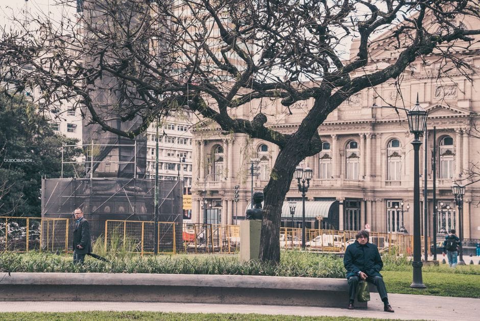 Pintoresco parque urbano con árboles y arquitectura histórica, gente interactuando.