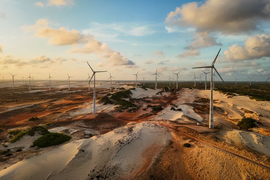 Toma aérea de turbinas eólicas en un extenso desierto al atardecer, capturando energía renovable.