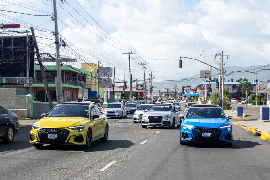 Escena callejera dinámica en Jamaica con automóviles coloridos circulando por una zona urbana vibrante.