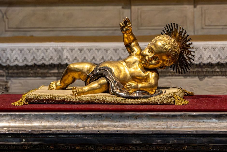 Estatua dorada adornada del Niño Jesús sobre un altar de terciopelo en una iglesia italiana.