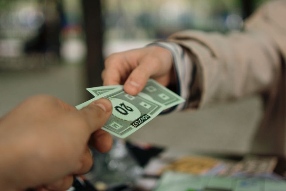 Primer plano de manos intercambiando dinero de Monopoly al aire libre en un parque.