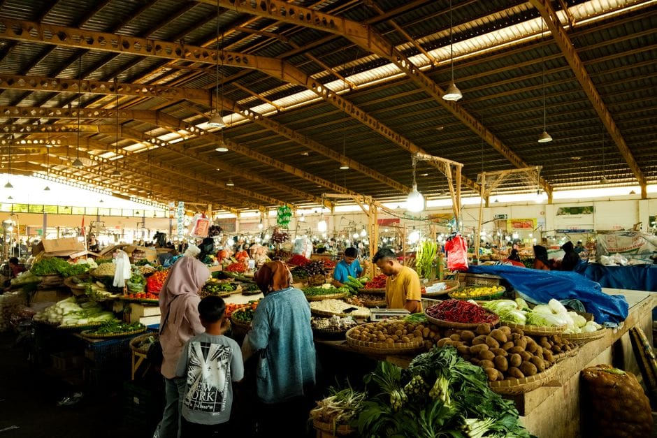 Un animado mercado cubierto con una gran variedad de frutas y verduras frescas expuestas bajo un techo de madera.