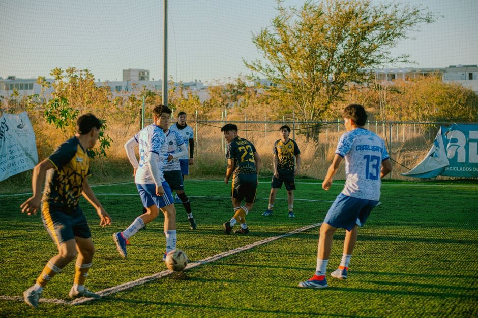 Los jugadores de fútbol adolescentes compiten en un campo al atardecer, mostrando energía vibrante y trabajo en equipo.