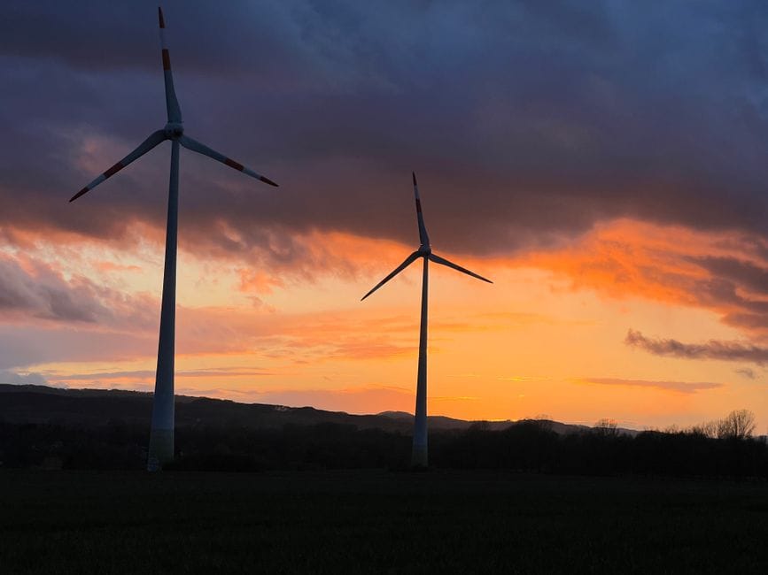 Aerogeneradores recortados contra una vibrante puesta de sol en la Alemania rural, que muestran la energía renovable.