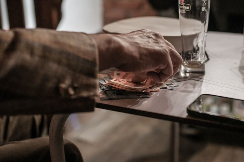 Mano contando billetes de euro sobre una mesa al lado de un teléfono y un vaso vacío.