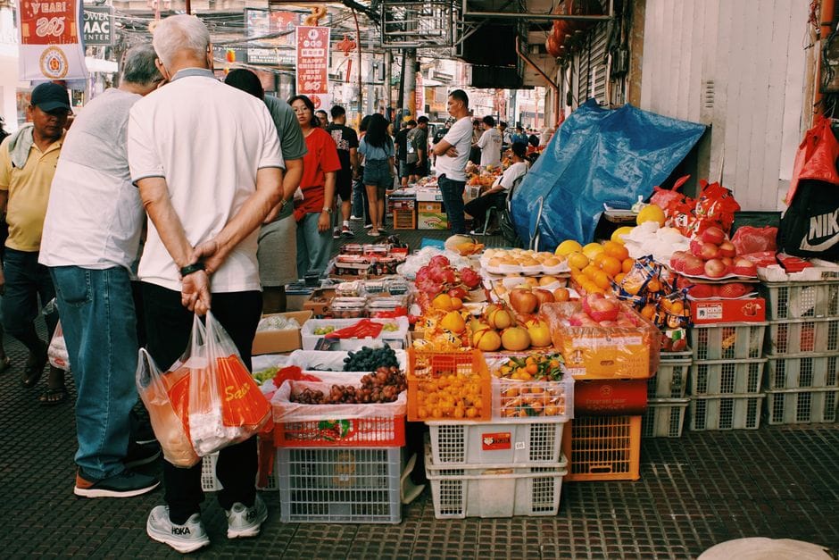 Mercado callejero animado con frutas diversas y gente animada en un entorno urbano.