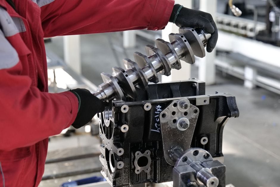 Mecánico trabajando en la instalación de un cigüeñal en un bloque de motor en un entorno industrial.