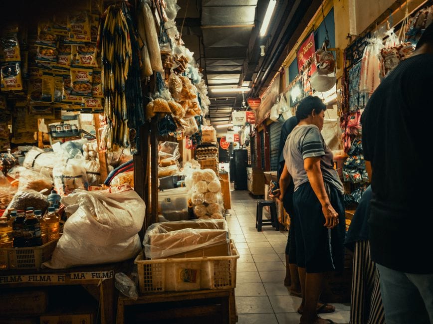 Un concurrido mercado interior con diversos productos y compradores explorando los pasillos.