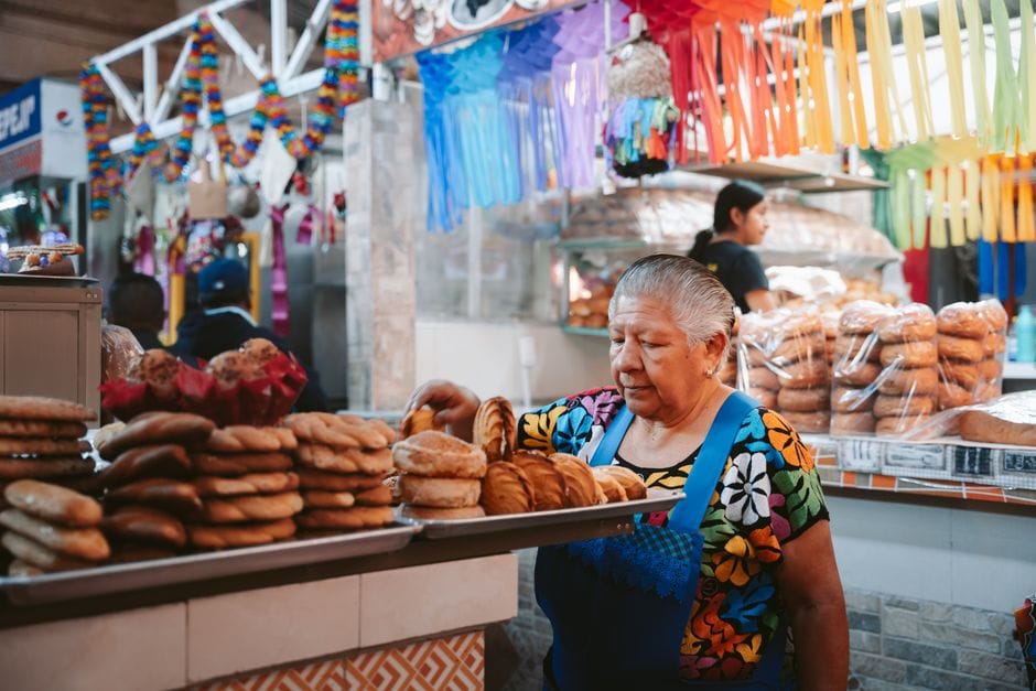 Mujer mayor trabajando en un vibrante puesto de panadería en el mercado de Oaxaca, México.