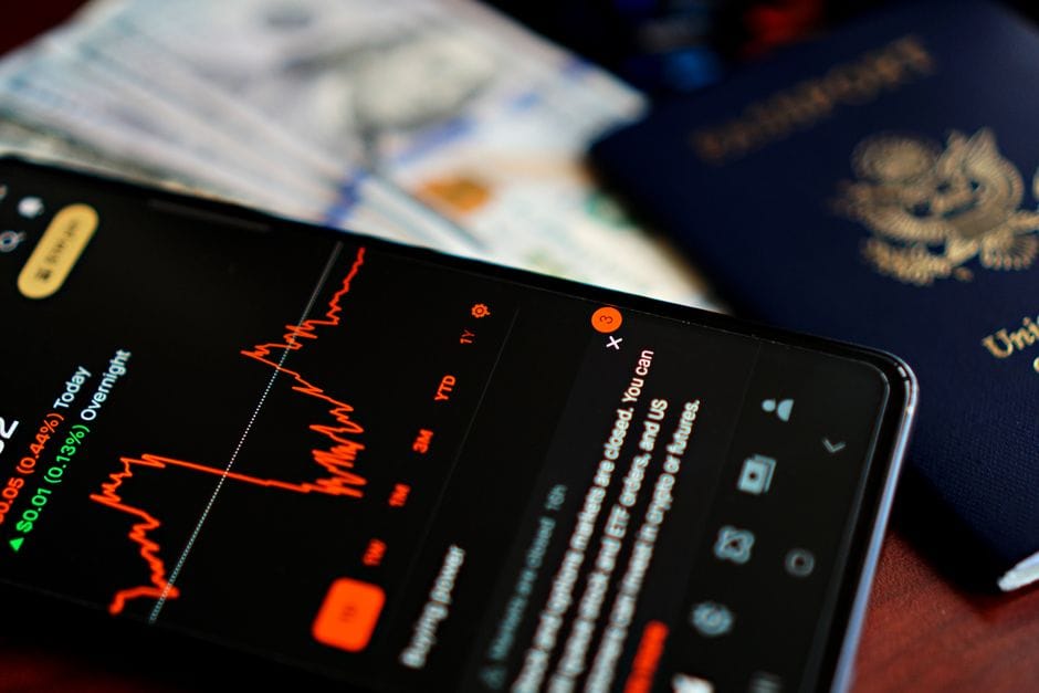 Primer plano de un teléfono inteligente que muestra una aplicación del mercado de valores junto a un pasaporte y una moneda estadounidenses.