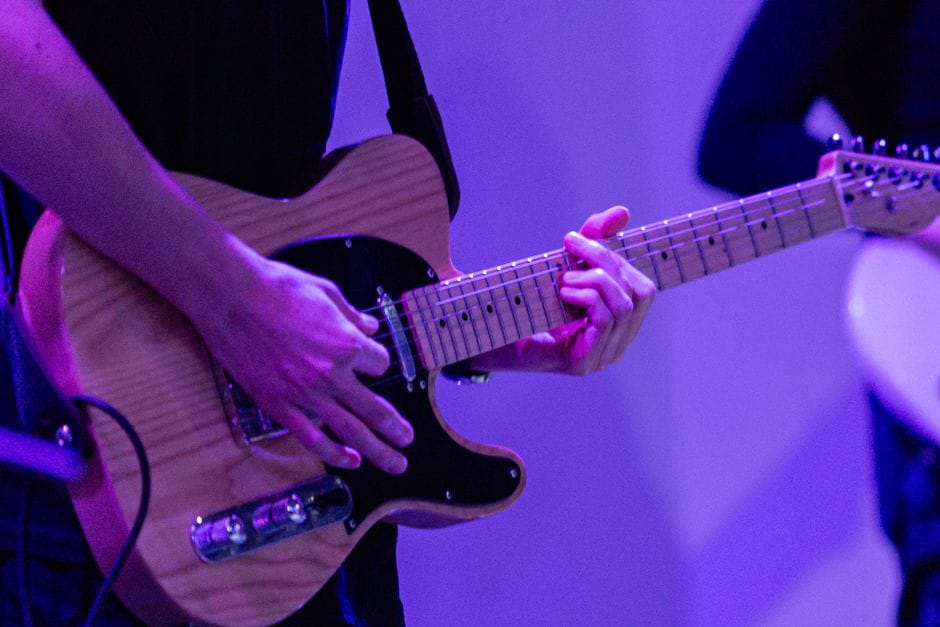 Músico tocando una guitarra eléctrica en el escenario con un fondo azul.