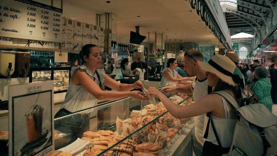 Clientes comprando pasteles en el bullicioso Mercado Central de Valencia, España.