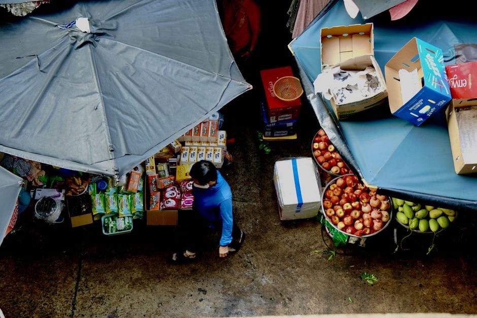 Fotografía cenital de un mercado con frutas, verduras y un comprador caminando.