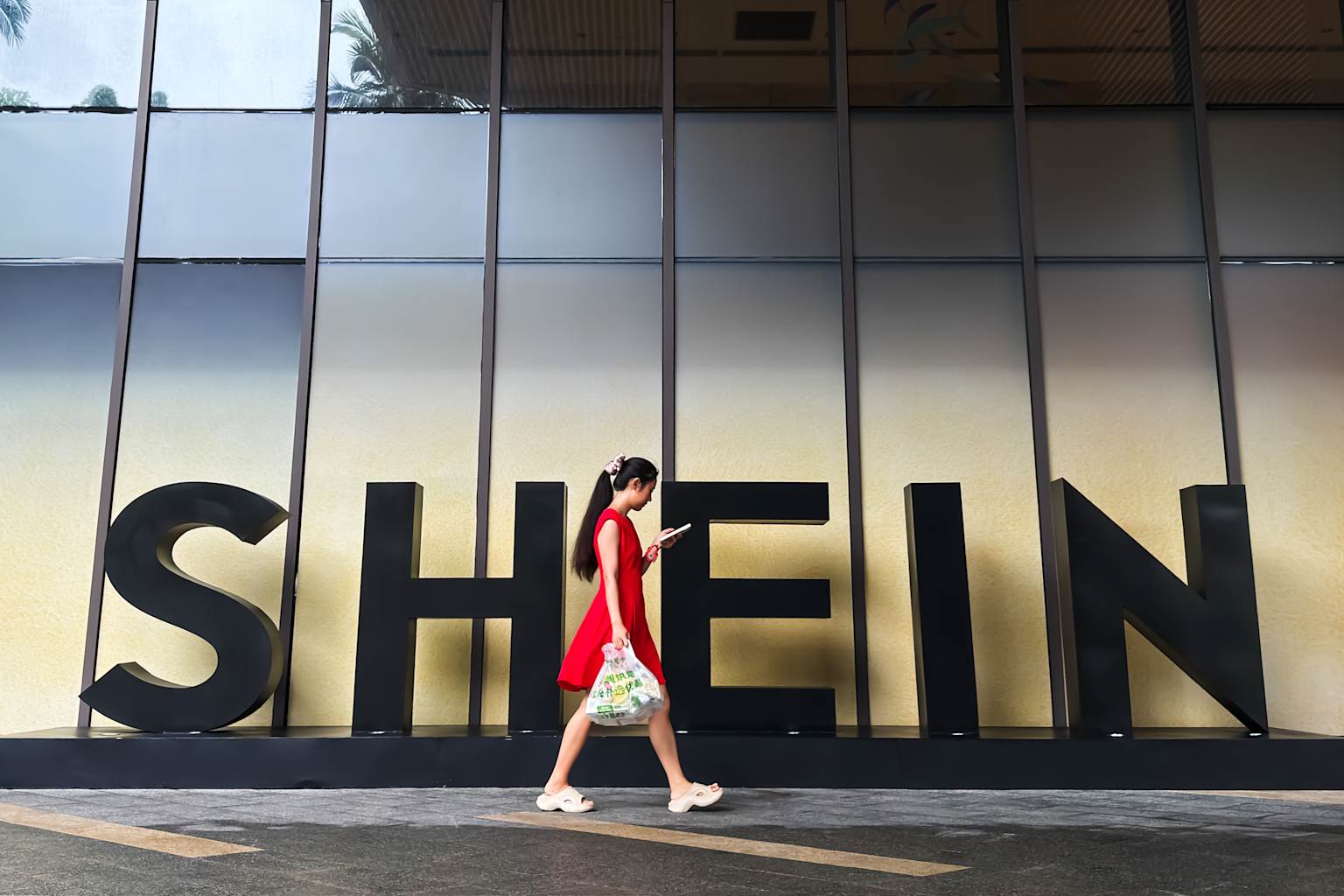 Una mujer mira su teléfono inteligente mientras camina junto a un anuncio de Shein