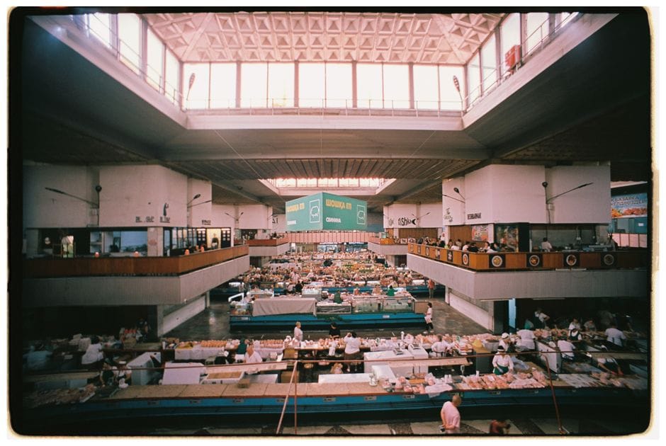 Vibrante escena de mercado interior en un entorno arquitectónico geométrico con puestos diversos y mucha actividad.