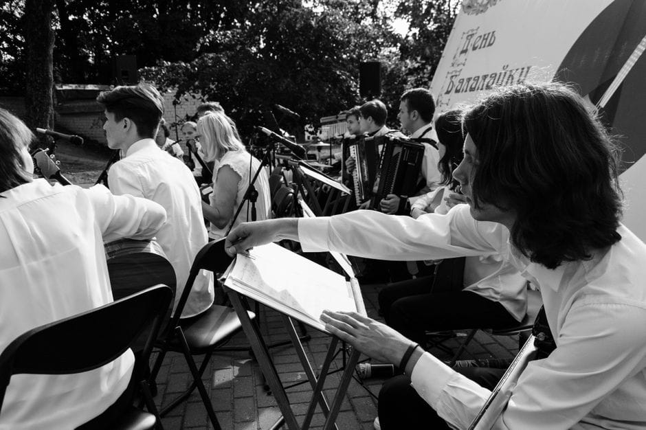 Actuación orquestal al aire libre con músicos tocando diversos instrumentos en blanco y negro.