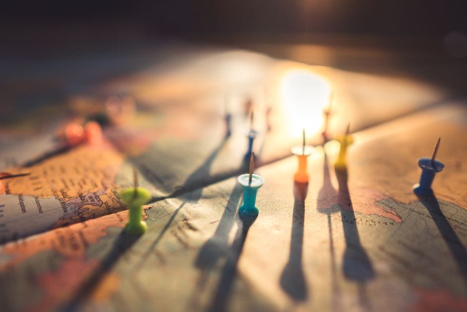 Una vista en primer plano de chinchetas coloridas proyectando sombras sobre un mapa mundial durante el atardecer, resaltando los viajes globales.