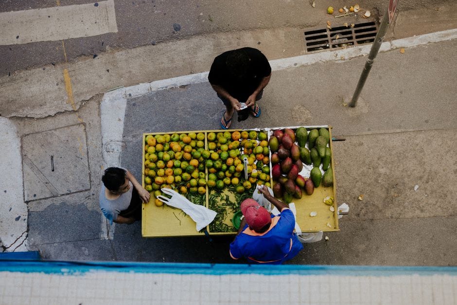Vista aérea de un vendedor ambulante que vende mangos y naranjas a dos clientes.