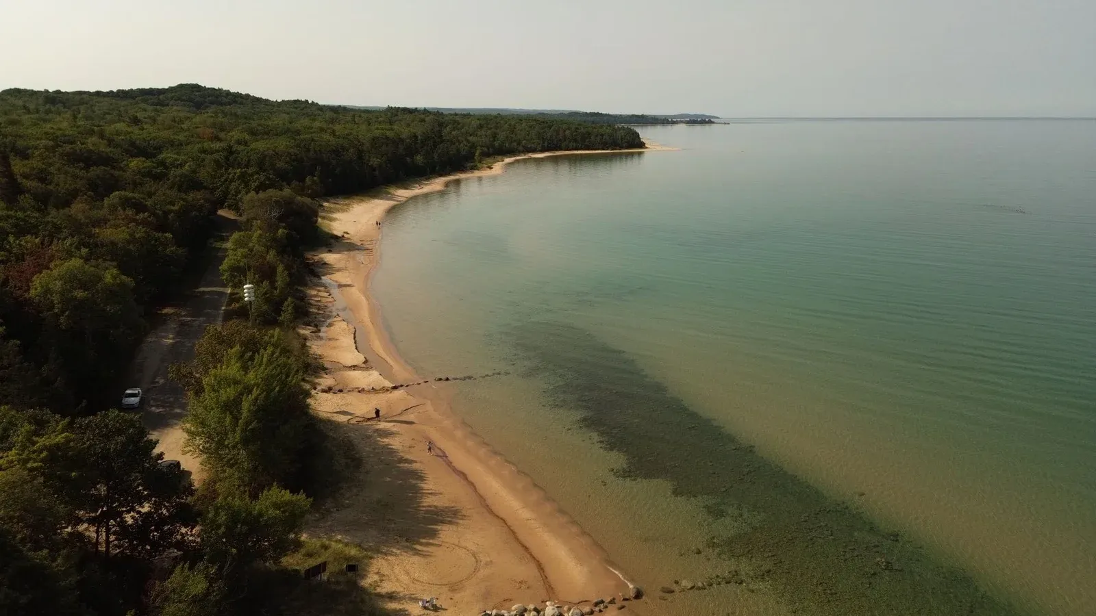 Aerial view of a serene beach and lush forest in Bliss, Michigan, showcasing the tranquil lake shore.