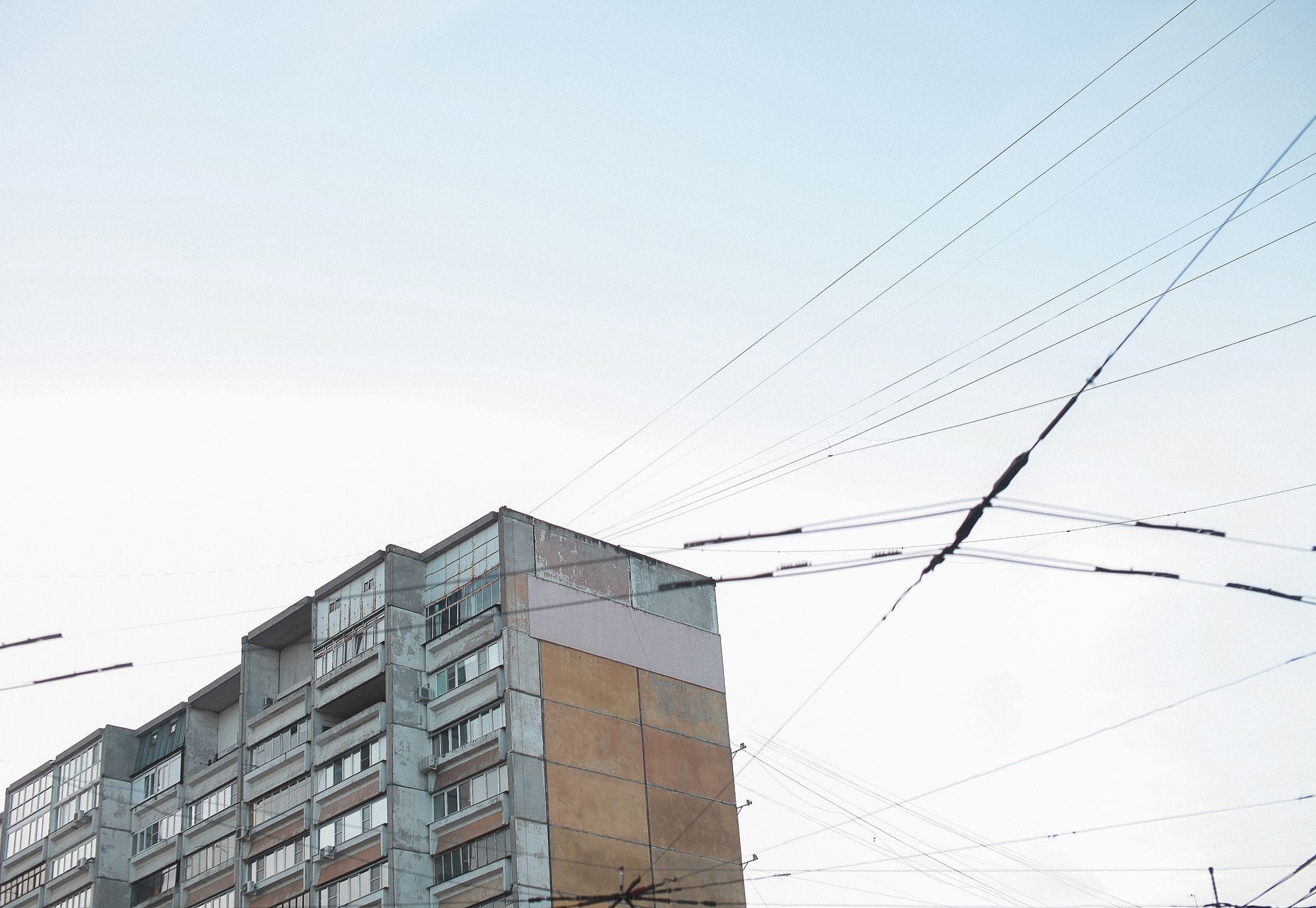 Cityscape view of an apartment building and power lines under a clear blue sky.
